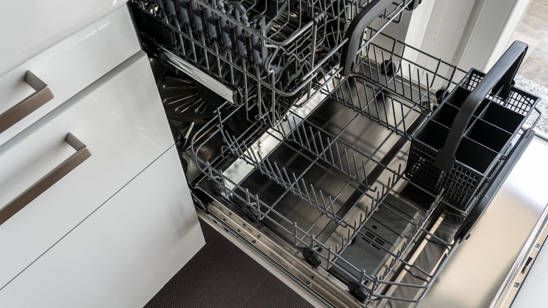 Open under-bench dishwasher with empty racks in a white kitchen
