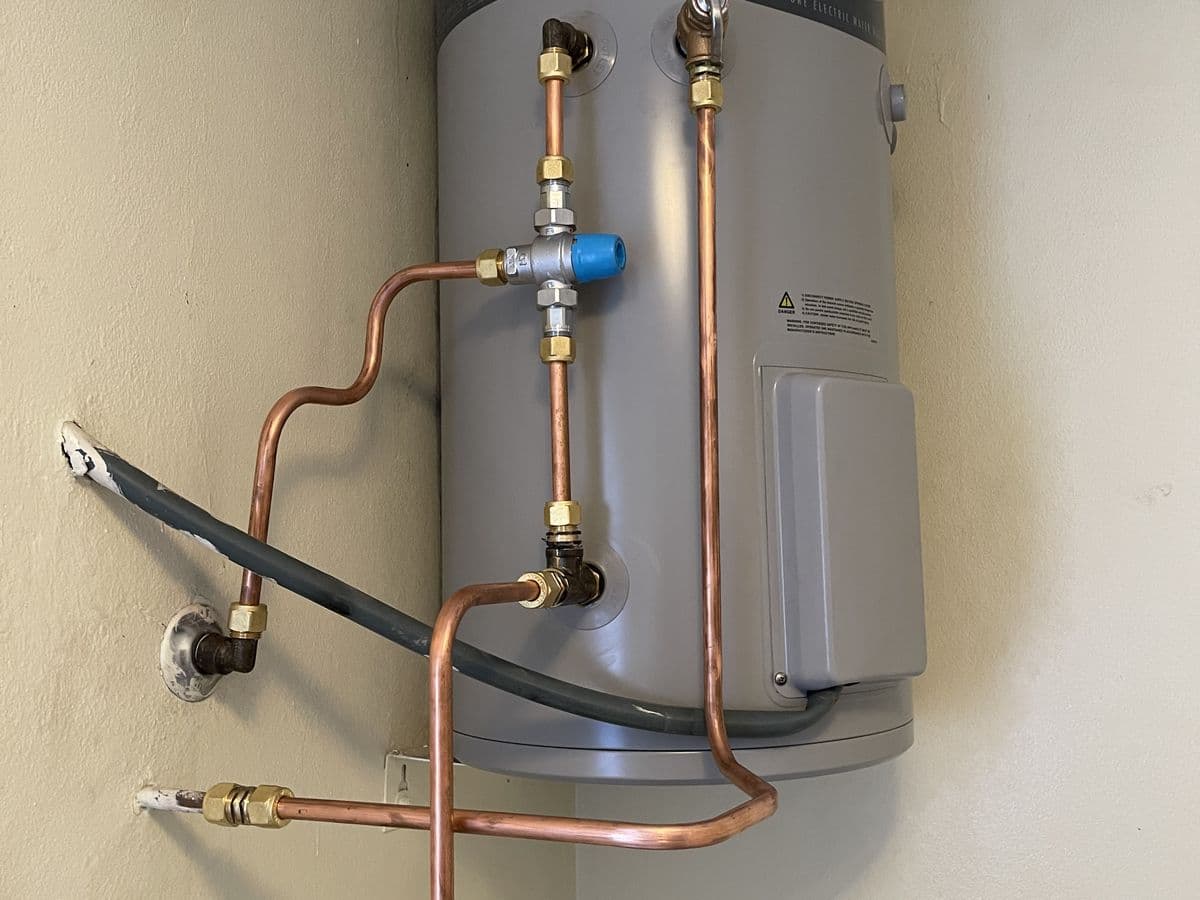 Electric storage hot water system mounted on a wall with copper pipework and a tempering valve