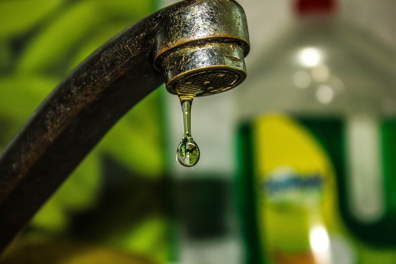 Close up of a dripping kitchen tap with water droplets falling into a sink